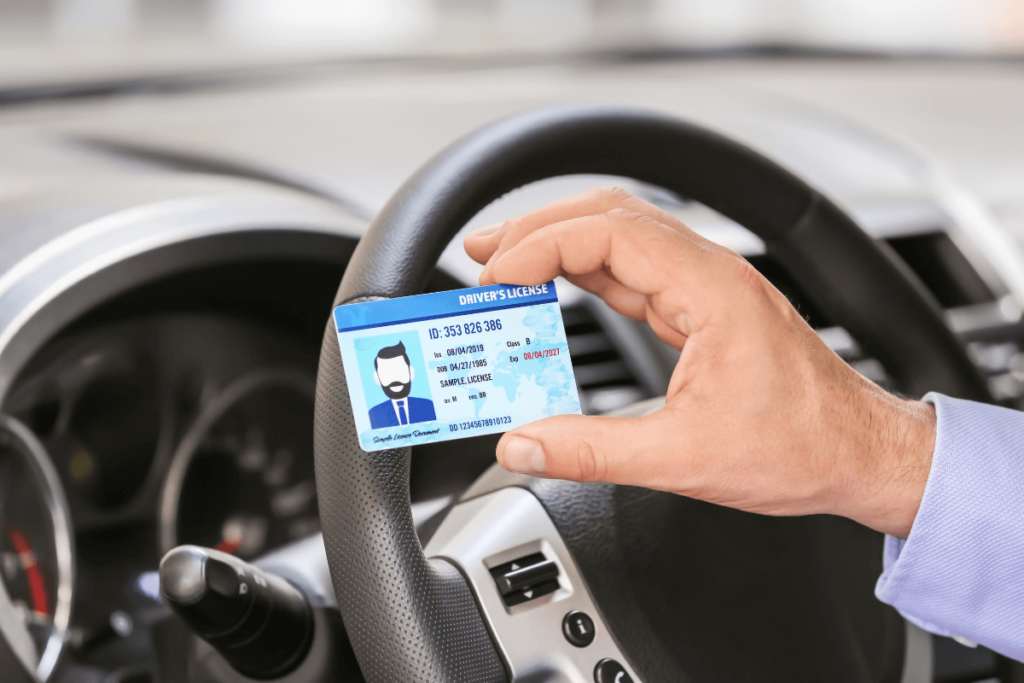 hand holding UK driving licence in front of a car steering wheel