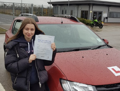  holding passed drivin license certificate in the UK in front of a red car