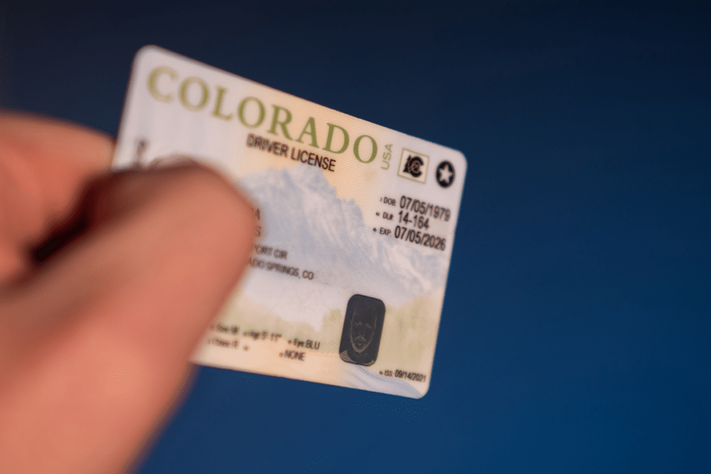 Colorado driver's license held in hand, addressing the question, "is my US driver's license valid in the UK?" for visitors driving for up to 12 months.